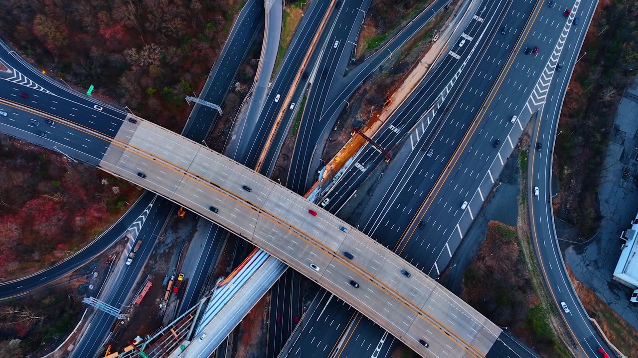 Crossing flyover bridges above a highway under construction, New Jersey. Top-down of intersecting elevated roadways with active bridge construction and equipment between traffic lanes