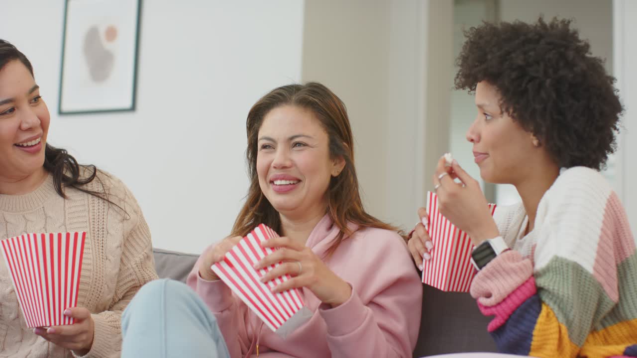 Forskellige veninder, der sidder i sofaen og spiser popcorn, reagerer på en joke og lugt uden for skærmen