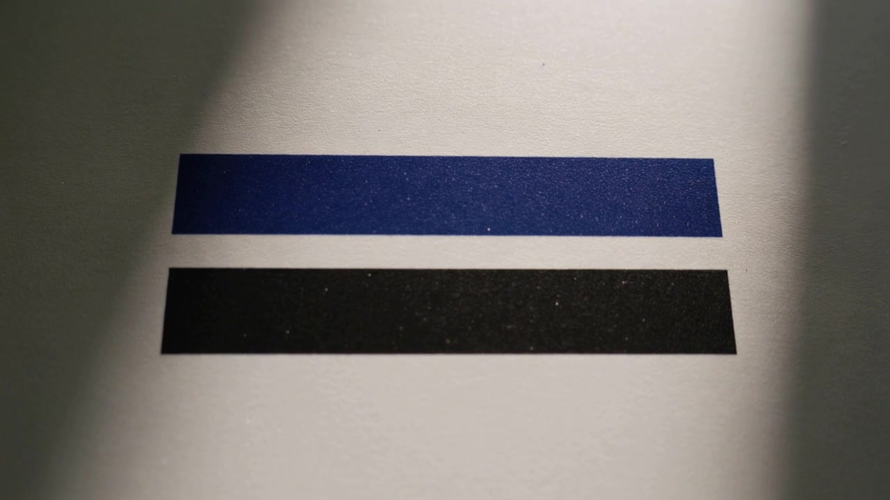 Shifting thin light source causing shadow bands softening across desk paper with blue black strips