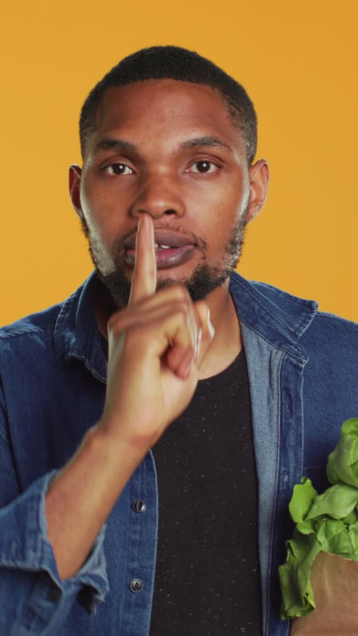 Young Man Shushing and Pointing While Holding Bag of Greens