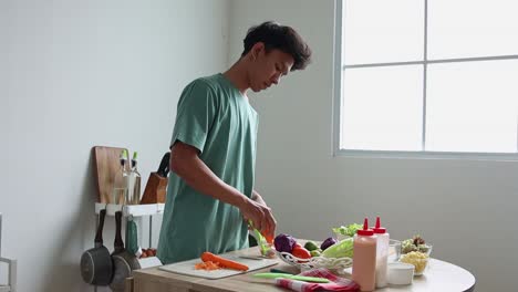 Young-Asian-Man-Grating-Fresh-Carrot-With-A-Grater-For-Salad-Ingredients,-Preparing-Dinner-At-Home