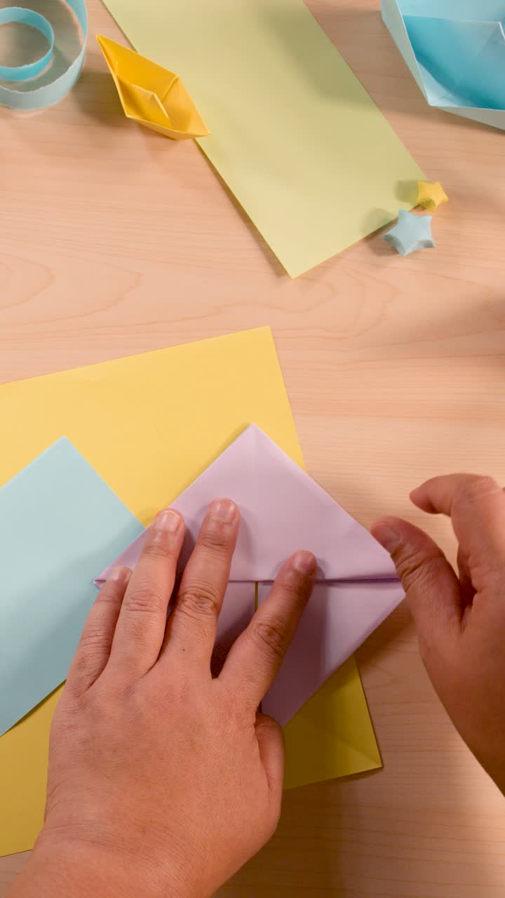 Mani adulte piegano carta pastello in origami, vista dall'alto, illuminazione soffusa, inquadratura stabile.