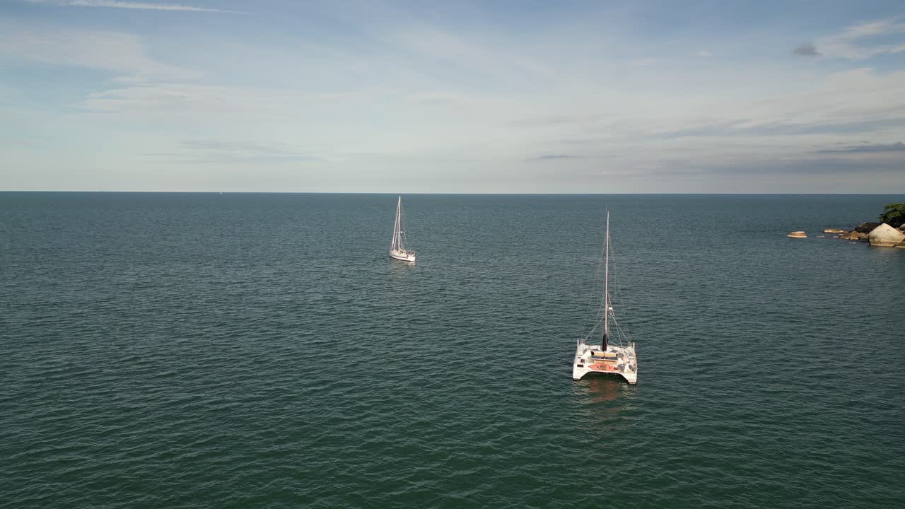 capturas de drones de un yate y barcos que navegan a través del agua del mar tranquila cerca de la costa rocosa