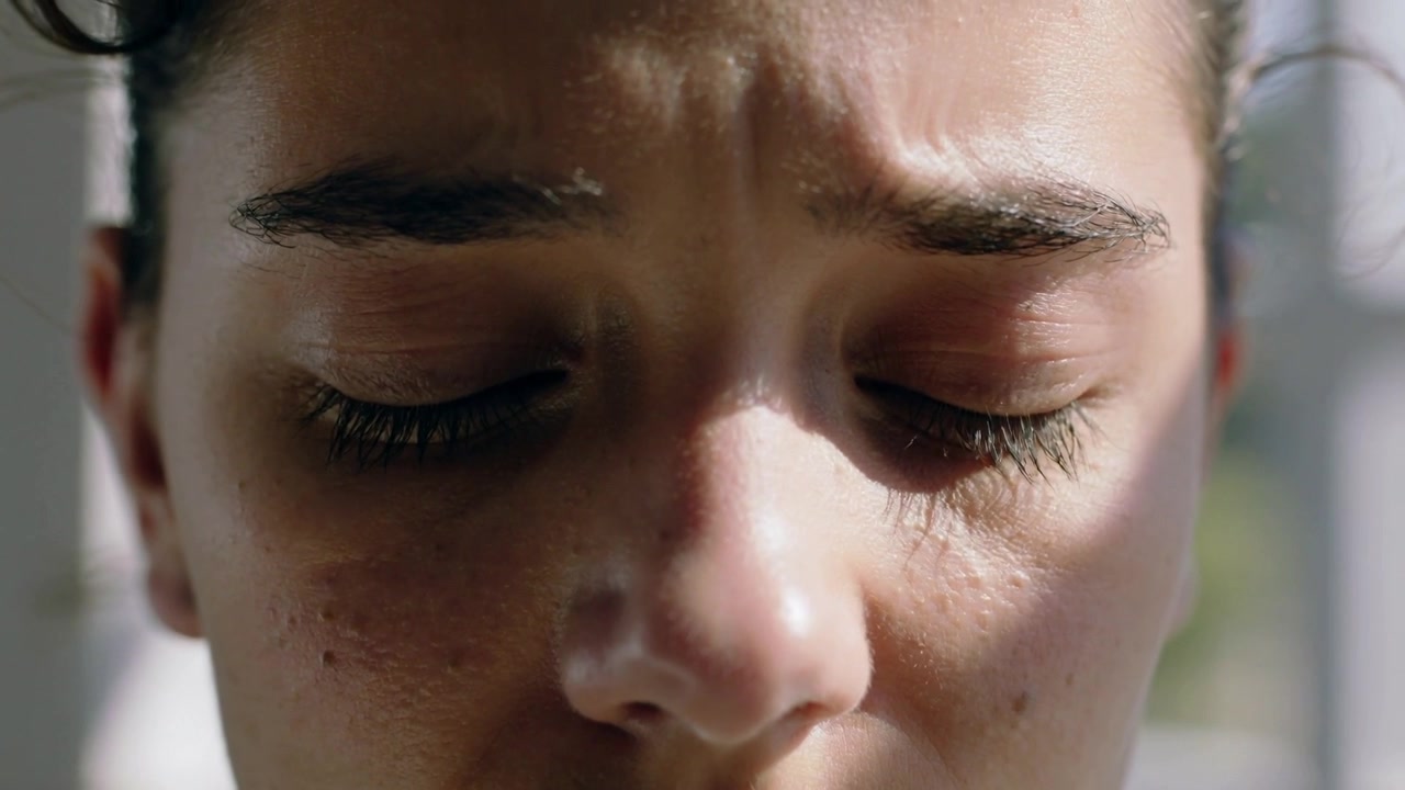 Blinking adult woman closing eyes slowly in room with vertical blinds, reacting to bright sunlight