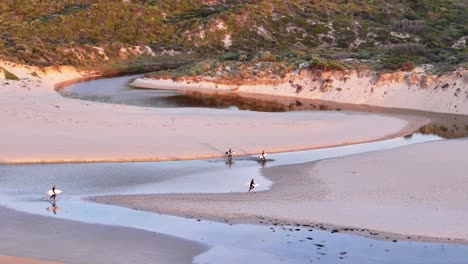 Surfistas-Al-Atardecer-Corriendo-A-Través-Del-Río-De-Regreso-Al-Aparcamiento-Después-De-Coger-Olas