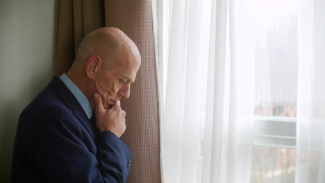 medium shot of a pensive thoughtful mature man looks out of a window