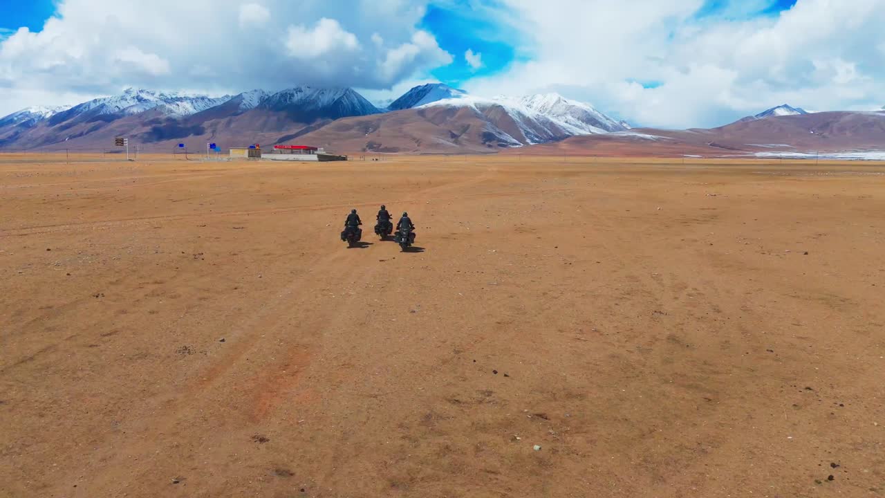 Aerial drone follows crew of motorcycle riders drive wild off road in the desert, with central Asian mountains background at daylight