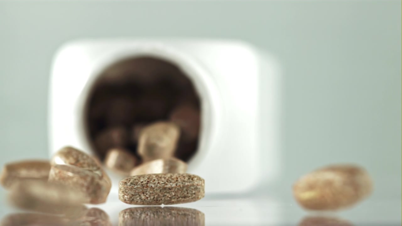Brown Pills Falling from a White Bottle in Slow Motion