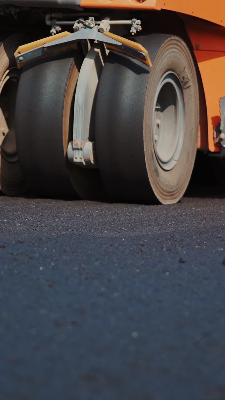 Modern asphalt roller machine stuck and press hot asphalt while making a new road. Big black wheels of a roller machine working on the new road. Vertical video