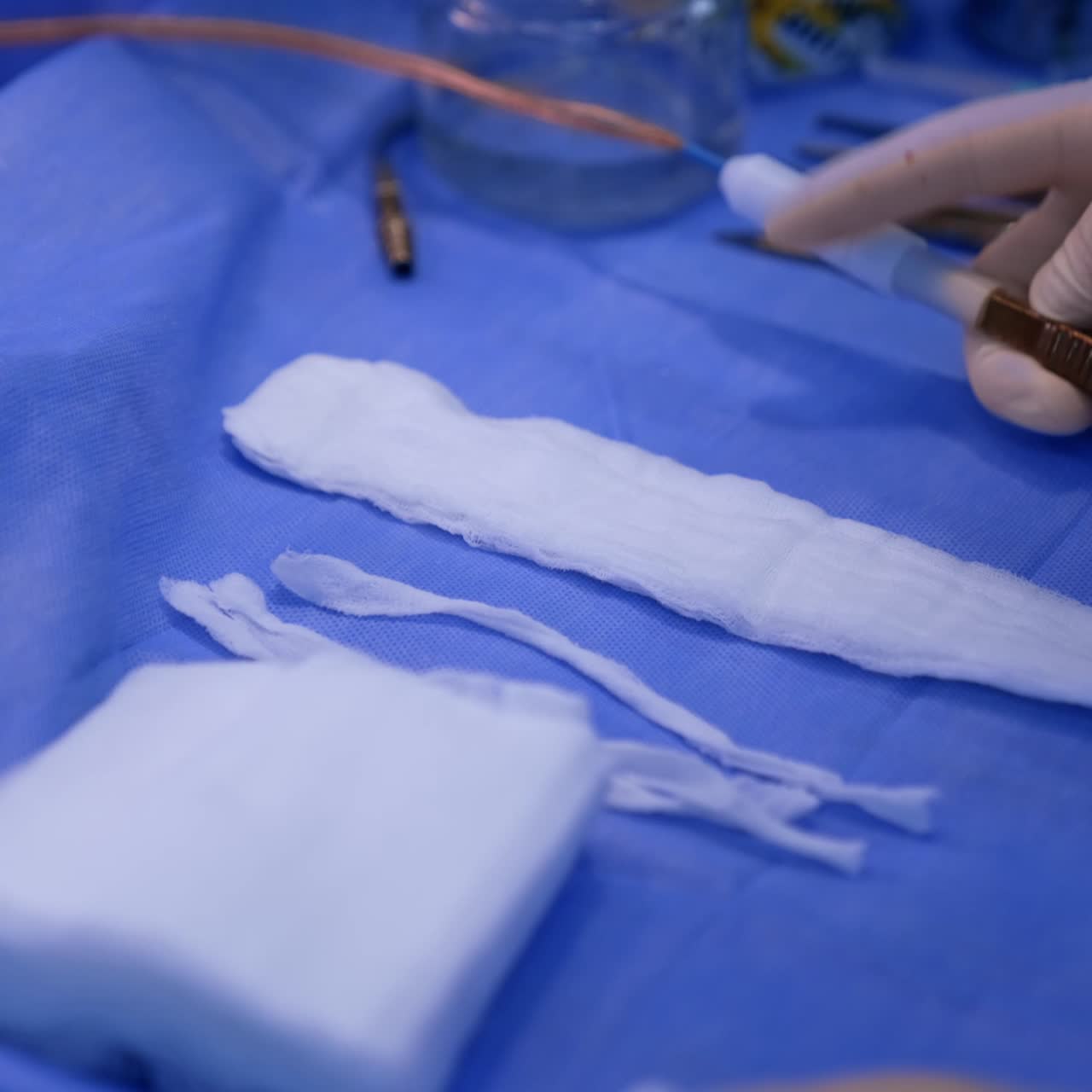 Bandages and tools prepared for operation. Hand in latex gloves holding electric forceps. Close up
