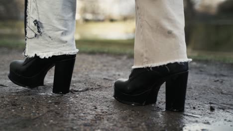 Young-woman-in-a-black-coat-walking-across-a-puddle-in-a-park-in-autumn-in-afternoon-1