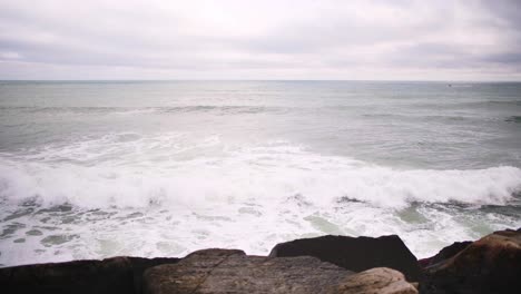 Vista-Aérea-De-Las-Olas-Del-Océano-Chocando-Contra-Las-Rocas-En-Un-Día-Nublado