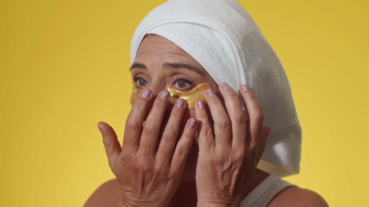 Gen X Woman Applying under Eye Patches on Yellow Background