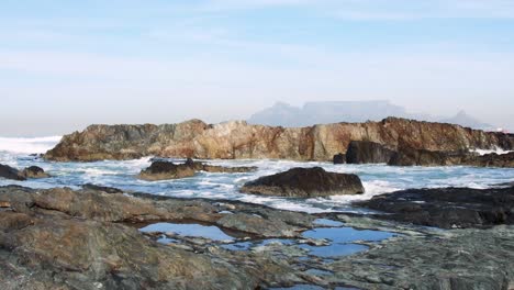 table mountain from behind a cluster of granite rocks on the edge of table bay on a beautiful morning.