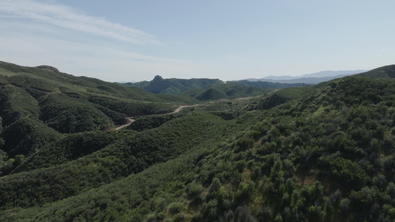 Picturesque aerial push-in shot of a lush green valley with a small winding road through the canyon with lots of vegetation on a sunny day
