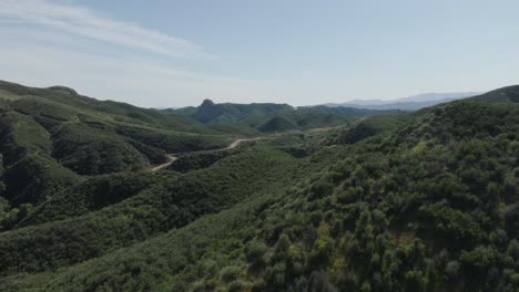 picturesque aerial push-in shot of a lush green valley with a small winding road through the canyon with lots of vegetation on a sunny day