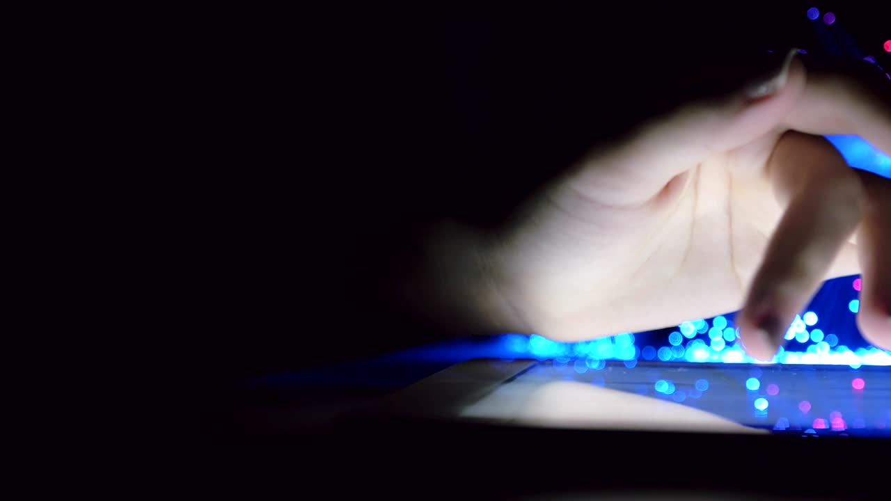 mujer tocando la mano y navegando en un dispositivo de tableta en una habitación oscura con luces de fibra óptica borrosas de colores movimiento de panorámica de primer plano