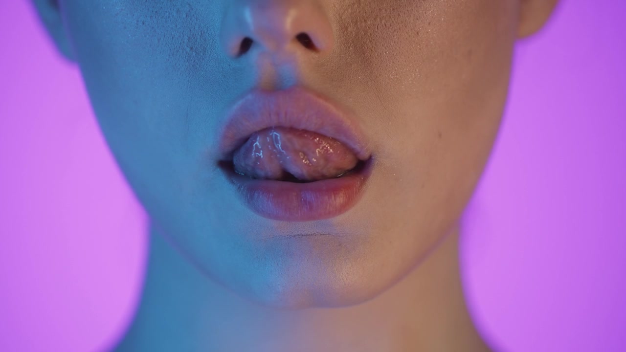 Primo piano della bocca di una donna che si lecca le labbra con la lingua, scatto in studio colorato