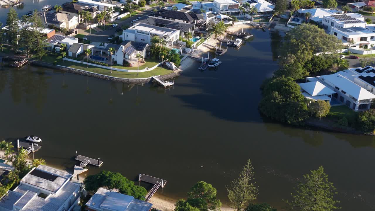 Aerial footage captures serene waterfront homes on Gold Coast, Australia. Bright daylight enhances the tranquil residential setting