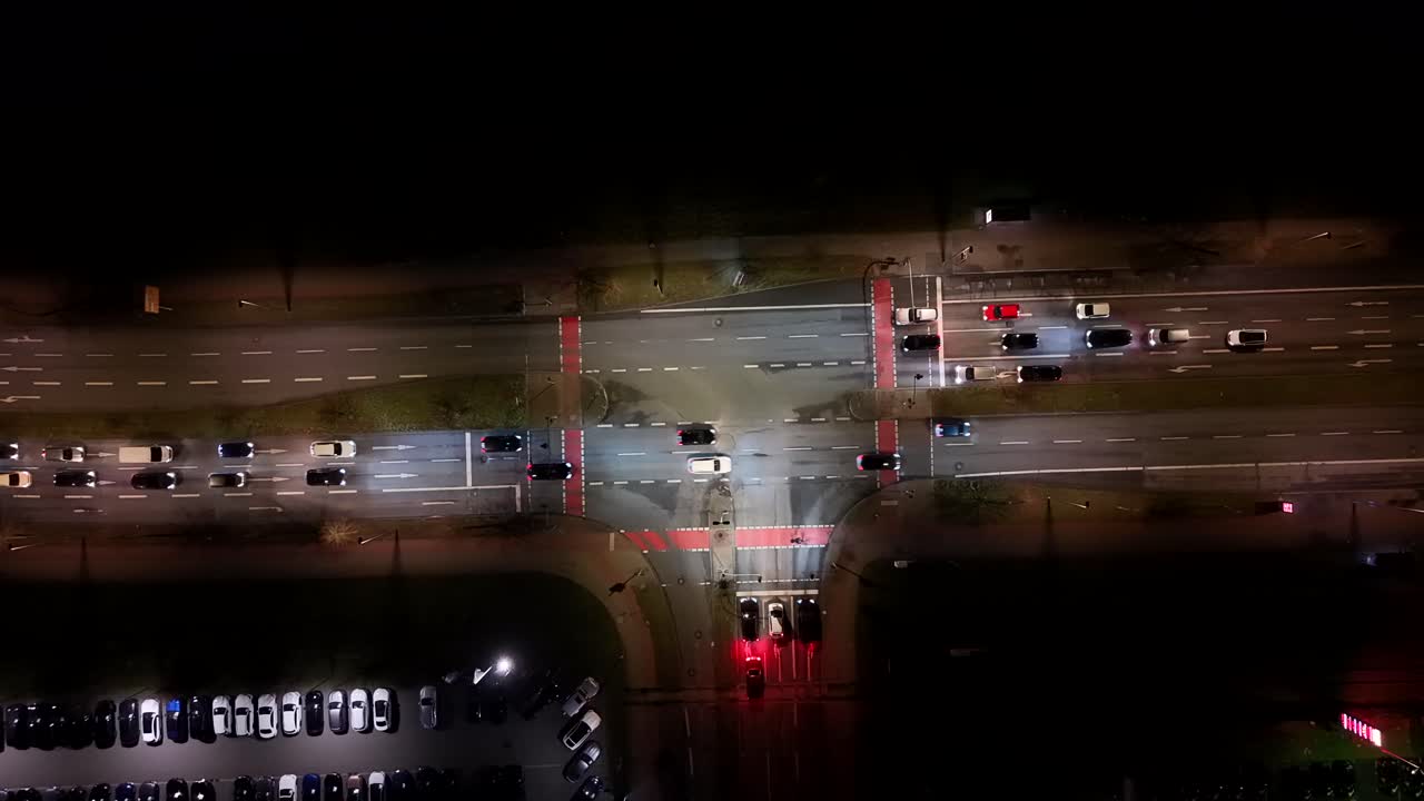 Traffic scene on junction of highway in American town. Driving cars on lighting street at night. Aerial top down shot