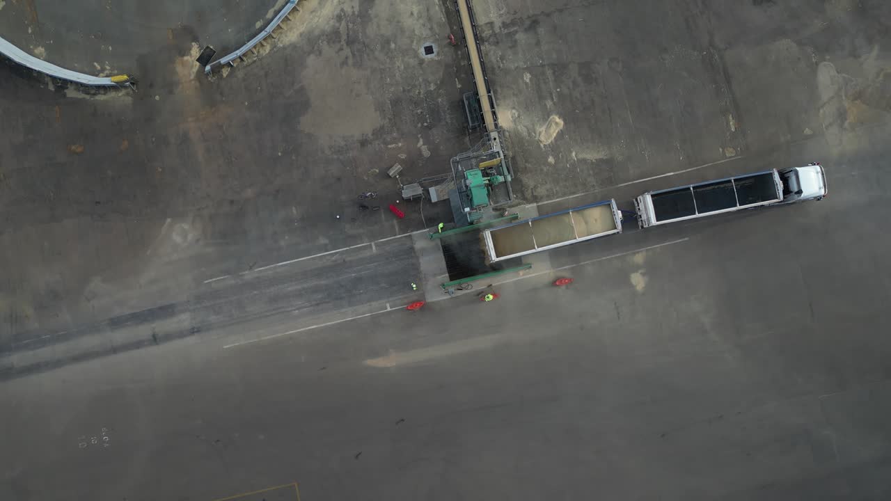 Cargo truck dumping grain into the pit on the ground with stockpile conveyor, aerial dynamic tilting down