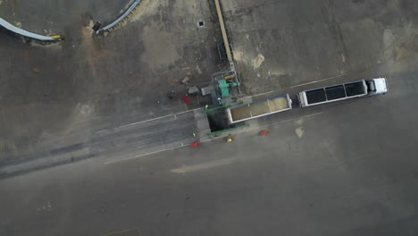 cargo truck dumping grain into the pit on the ground with stockpile conveyor, aerial dynamic tilting down