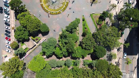 vista panorámica de la hermosa y verde plaza de la ciudad con una gran fuente en el medio mientras la gente se ocupa de sus asuntos
