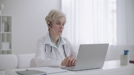 female head physician of hospital is communicating with doctors by online video conference at laptop sitting in her office