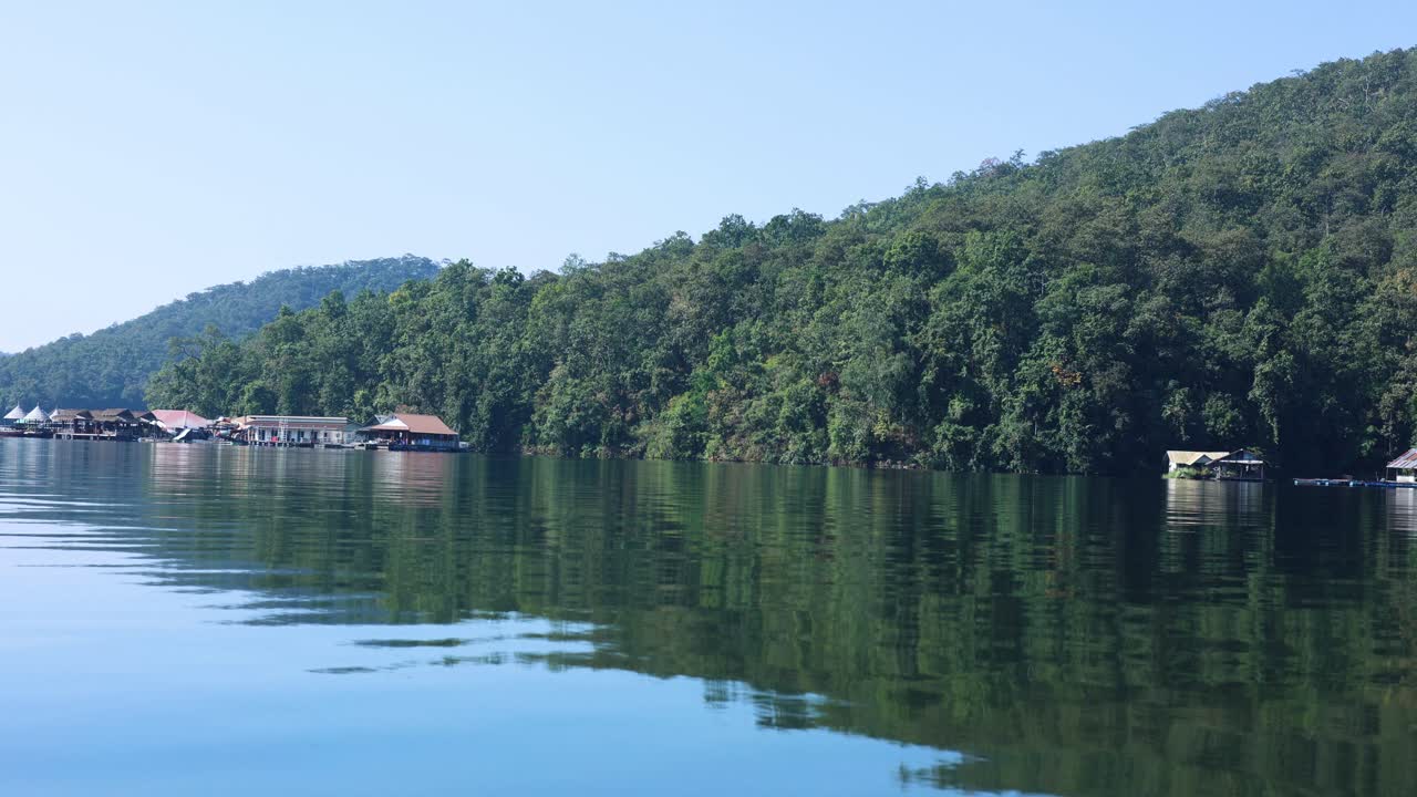 el agua tranquila refleja el bosque y las casas flotantes.