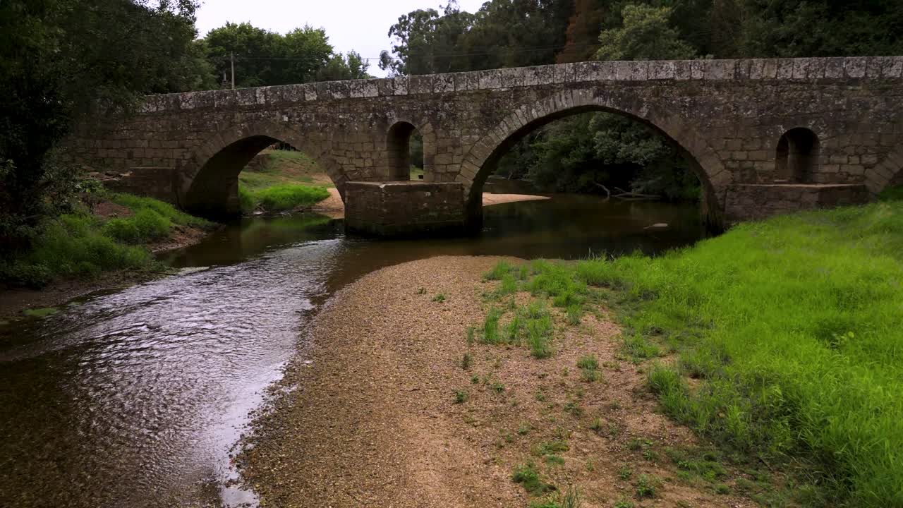 Historic stone bridge over serene river in Portugal's lush landscape