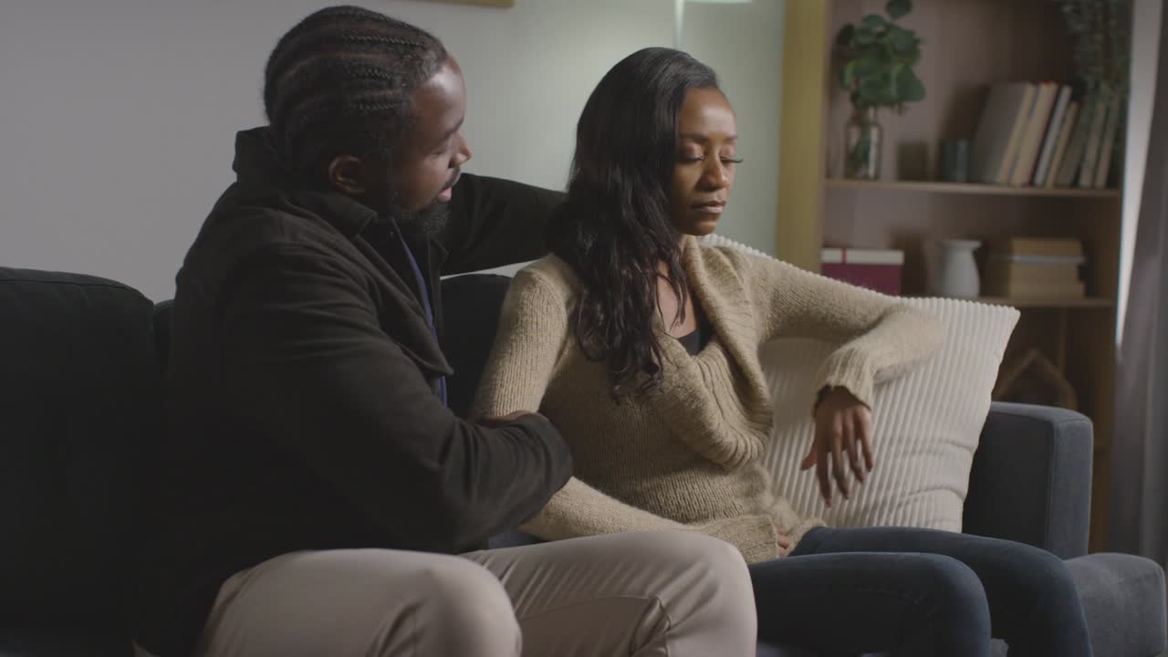 Couple At Home Sitting On Sofa In Lounge With Man Comforting Unhappy Woman 4