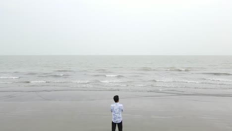hombre solitario fuerte y seguro de sí mismo de pie en la playa, disparo aéreo ascendente