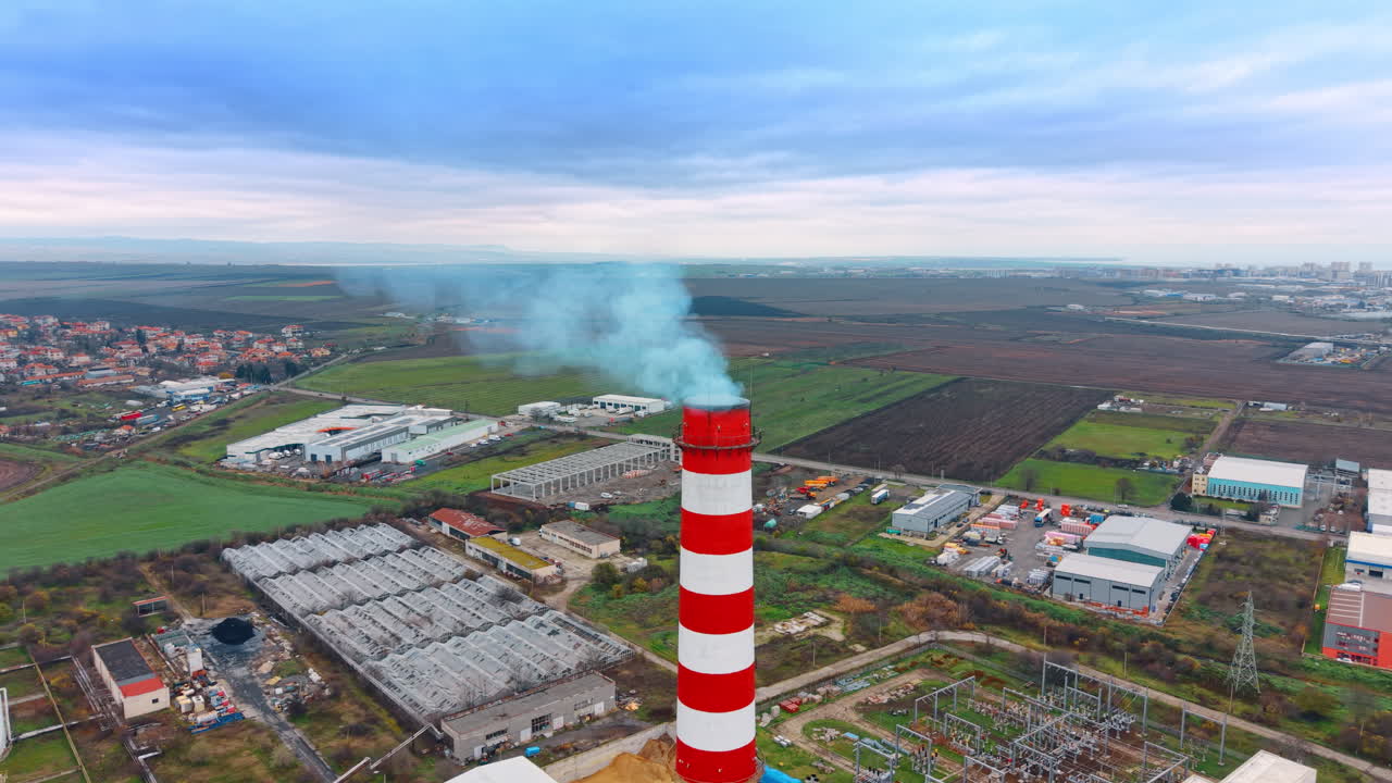Sottostazione elettrica e impianto industriale con camino fumante. Prospettiva aerea di una sottostazione elettrica ad alta tensione e di un impianto industriale con un'alta ciminiera fumante.