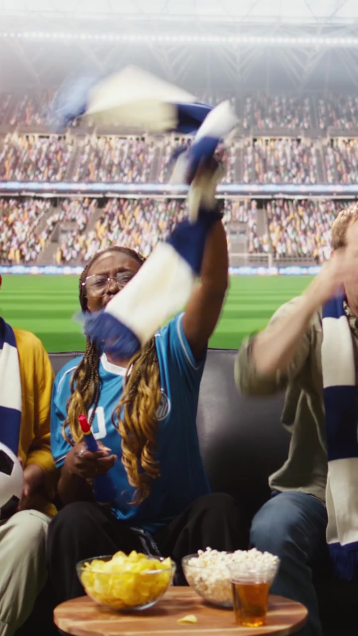 Video vertical. Apasionados aficionados al fútbol ven un partido en casa en una transmisión deportiva inmersiva