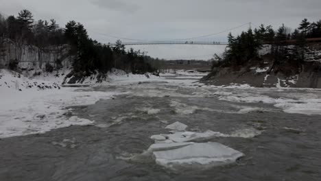 people crossing bridge above icy stream in chutes chaudiere canada - aerial shot