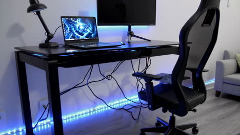 a gaming desk setup with blue led lighting, featuring a laptop and chair