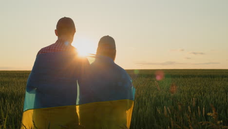 a young couple with the flag of ukraine on their shoulders looks at the sunrise over a field of wheat. hope and optimism concept