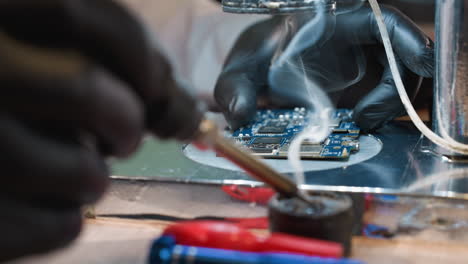 a close-up view of a technician using a soldering iron to repair a circuit board under a microscope, with some tools near by