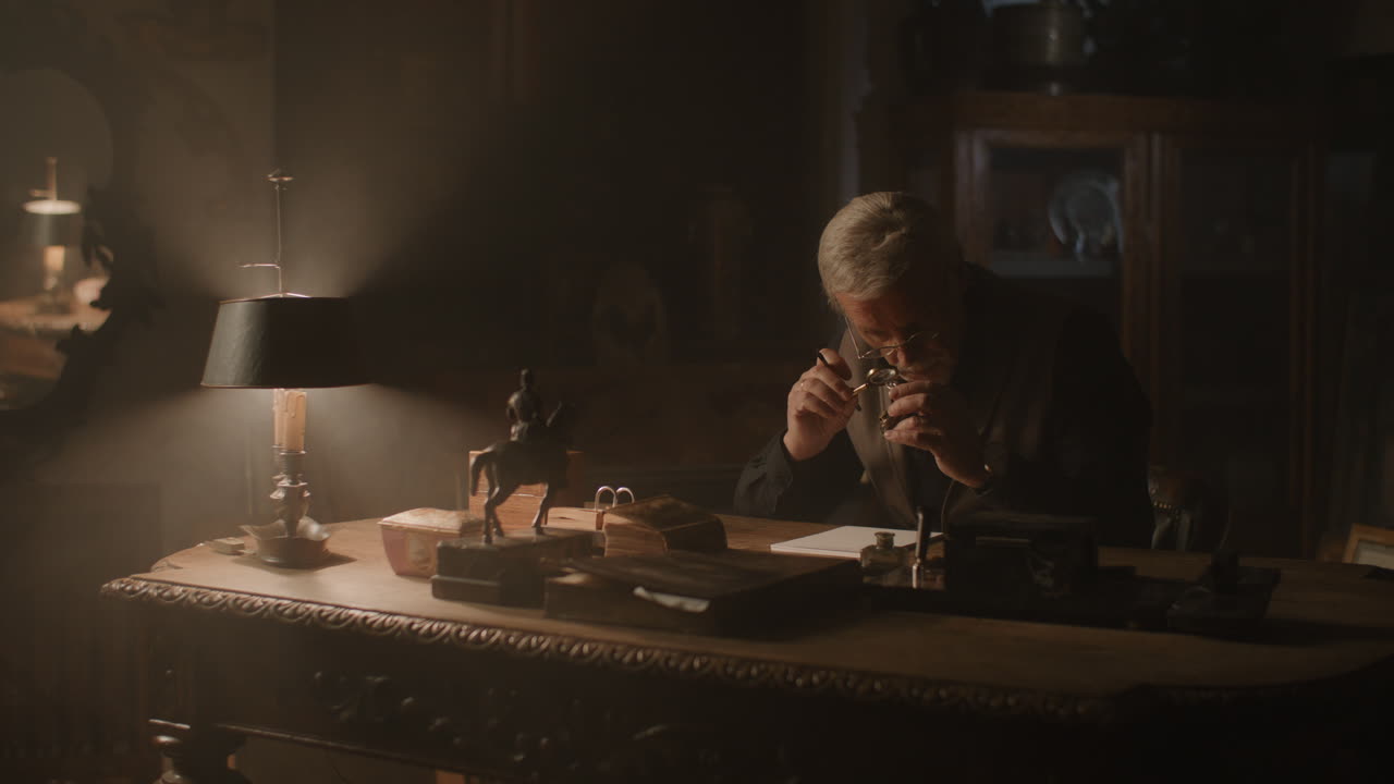 Older passionate man evaluates an old silver skull watch in his office at night