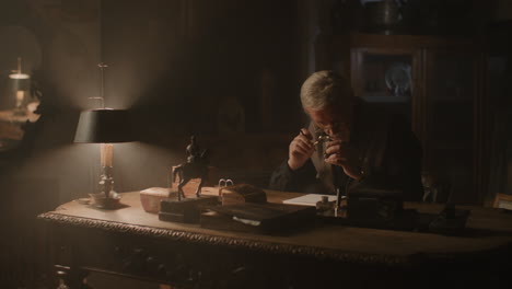 older passionate man evaluates an old silver skull watch in his office at night