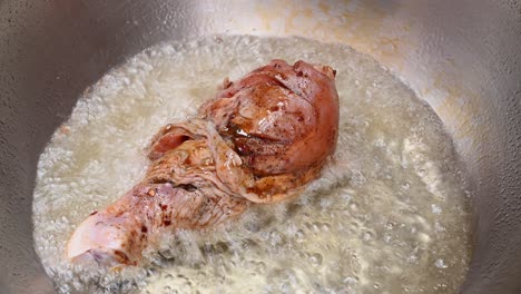 aceite ya hirviendo, una mano con pinzas agarra la carne y deja caer el trozo de pollo y luego otra, el aceite chisporrotea