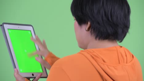 Back view shot of Asian woman using digital tablet with copy space chroma key against green background