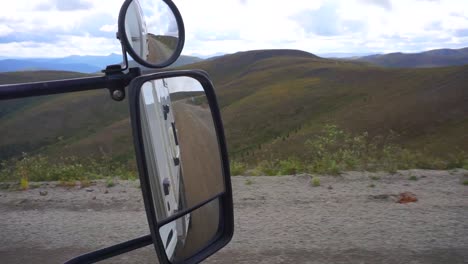 static view looking at a mirror, while driving on the top of the world highway, inside a camper van, up in the yukon highlands, on a cloudy day, in canada