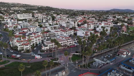 a dynamic drone push-in shot of the san clemente pier bowl neighborhood, highlighting spanish-style architecture, palm trees, and proximity to the beach. captured at twilight.