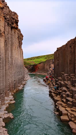 tourists walk by the rocks near the narrow river. beautiful columnar mountains in iceland. vertical video.
