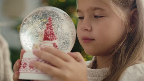 un primer plano de una niña caucásica sosteniendo y mirando fijamente una bola de nieve.
