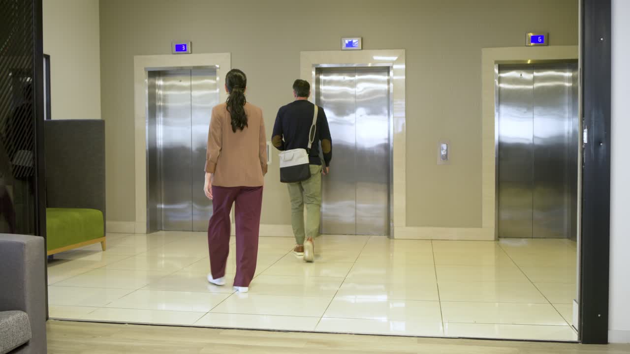 Diversos colegas de trabalho chegando ao conjunto de elevadores no escritório e apertando o botão de chamada após discutir a escolha