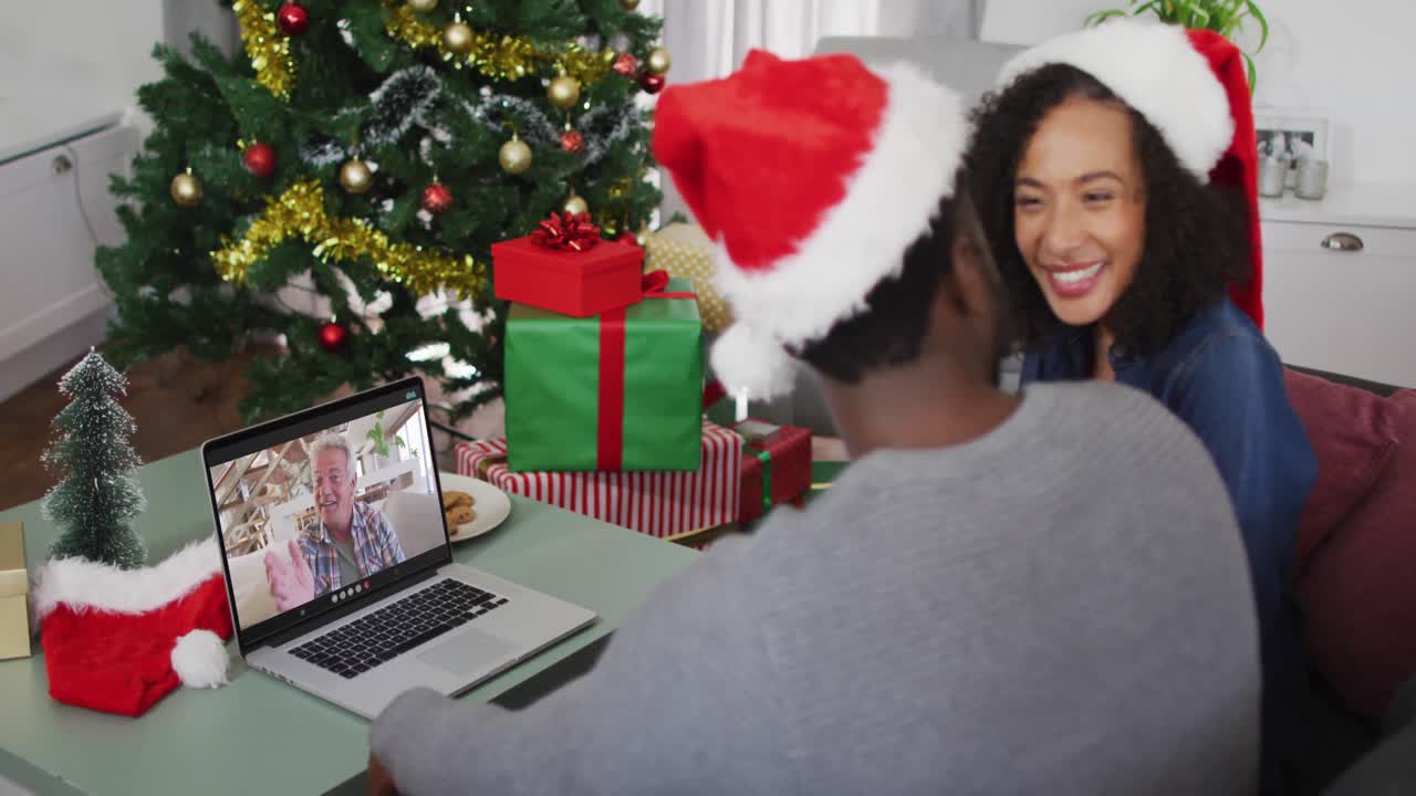 pareja afroamericana con sombreros de santa haciendo una videollamada en una computadora portátil en casa durante la navidad