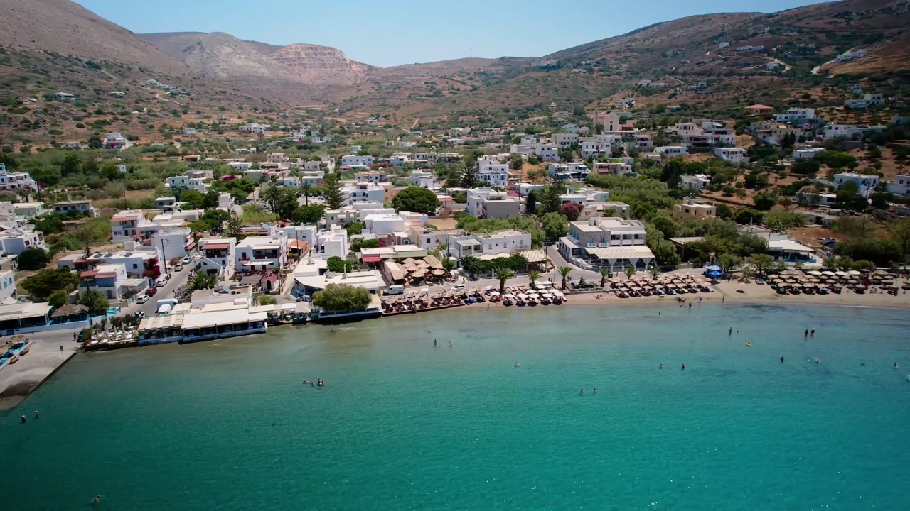 Aerial footage of a coastal town with a sandy beach and clear turquoise water in greece