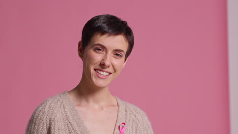 retrato de estudio de una joven sonriente que lleva una cinta rosa de concienciación sobre el cáncer de mama contra un fondo rosa